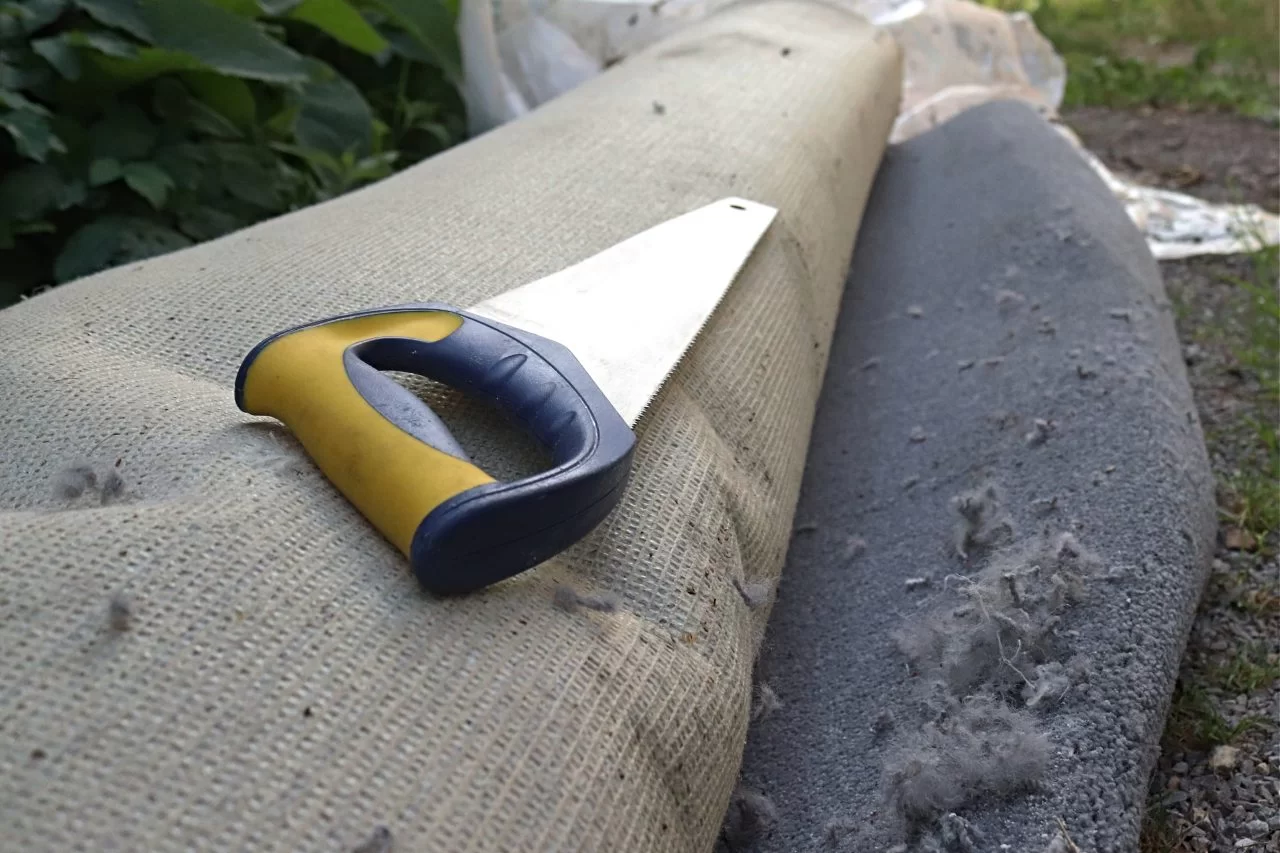 grey rolled carpet with handsaw lying on top